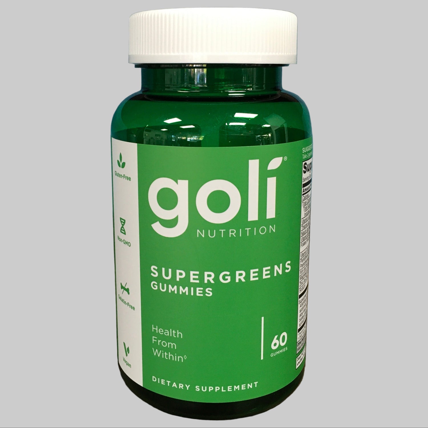 Green bottle of goli Supergreens Gummies on a wooden surface with a blue background