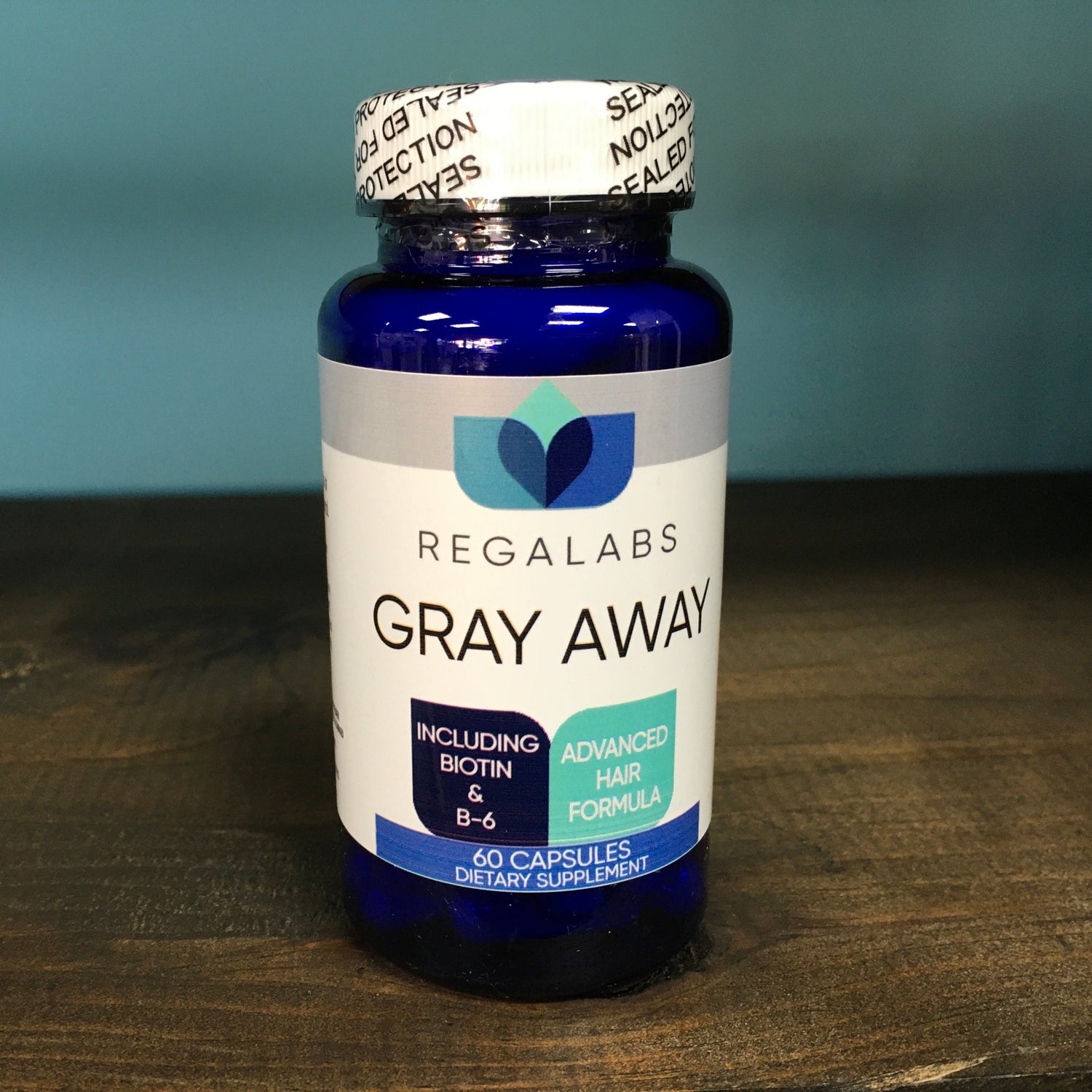 Bottle of Regalabs Gray Away supplement on a wooden surface with a blue background